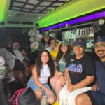 Group of friends and family smiling inside a party bus decorated with baseball balloons and Happy Birthday banner.