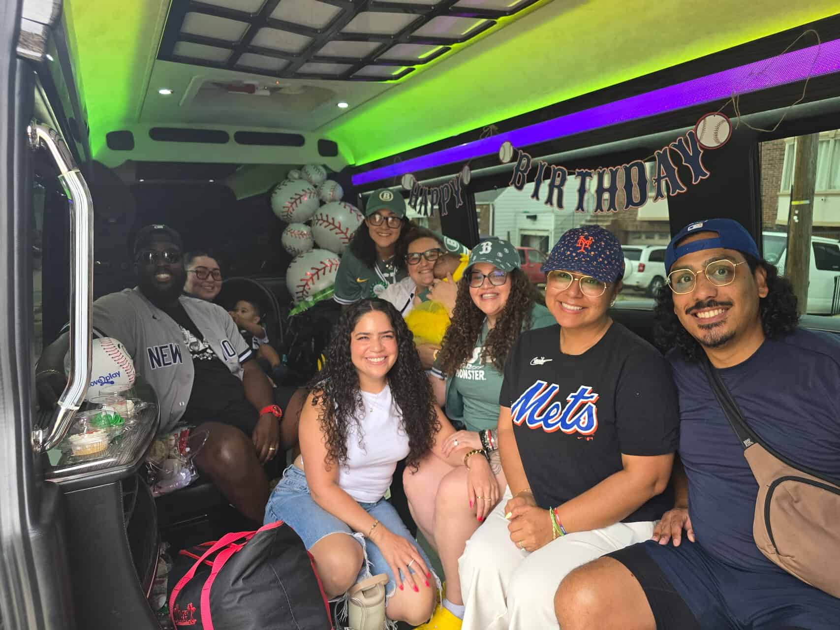 Group of friends and family smiling inside a party bus decorated with baseball balloons and Happy Birthday banner.