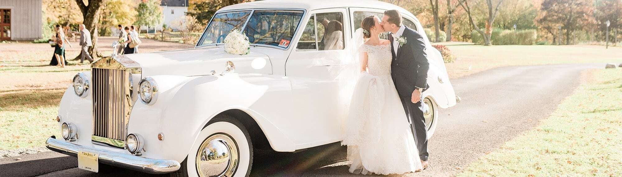 Wedding couple kissing beside vintage Rolls Royce in autumn — Moonlight Limo wedding limo service Glen Rock NJ